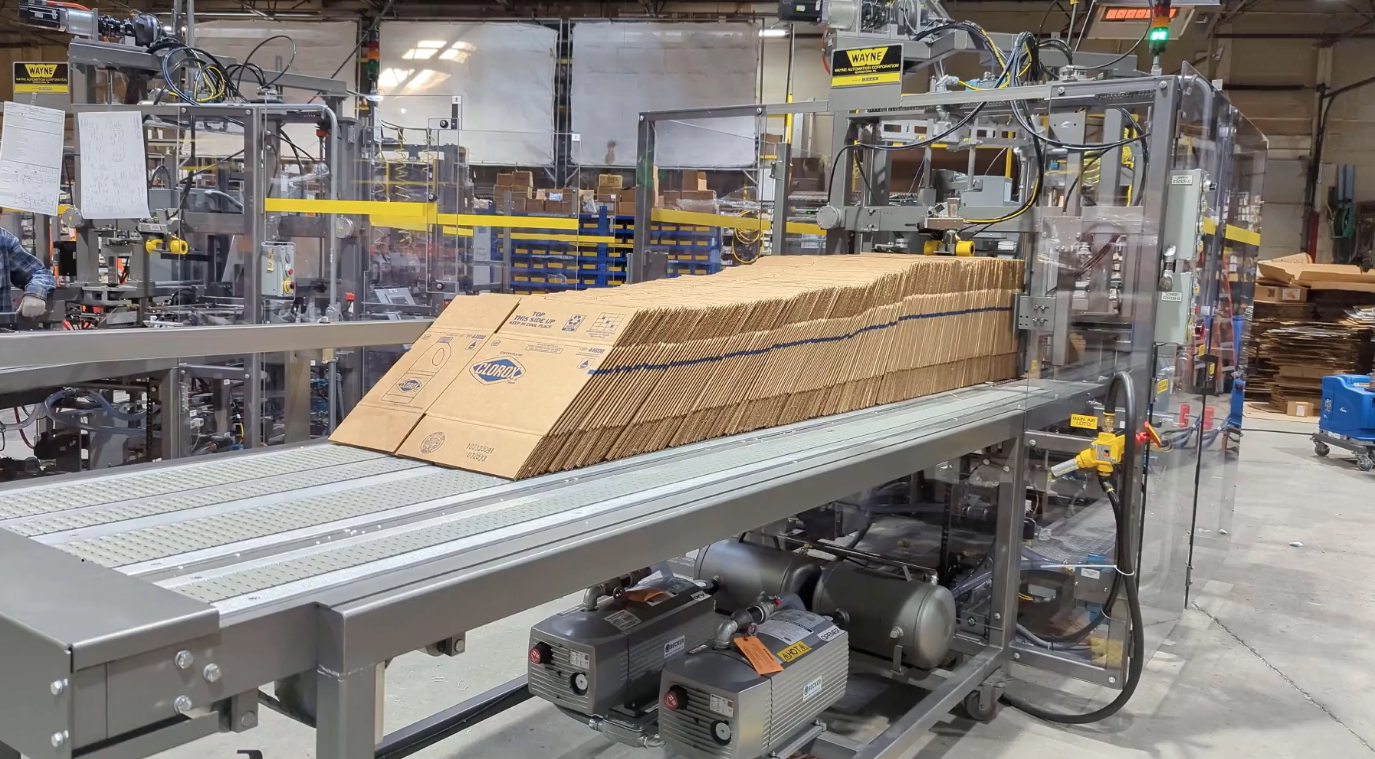 A stack of corrugated boxes feeding into a case erector for high-volume chemical packaging operations.